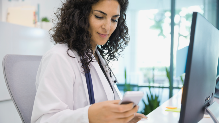 A photo of a health care practitioner using a desktop and mobile phone