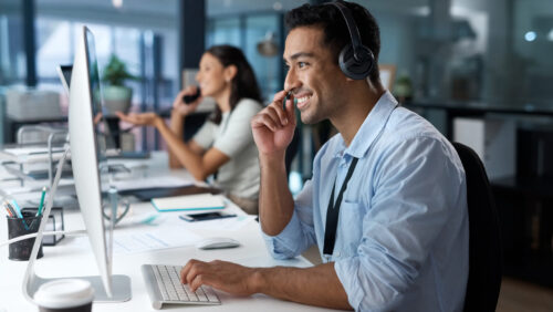 customer service agent smiling while wearing a headset at a computer